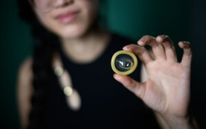 Ami, a young asian woman, holding a condom between her fingers, with the focus on the condom and a blurred background.